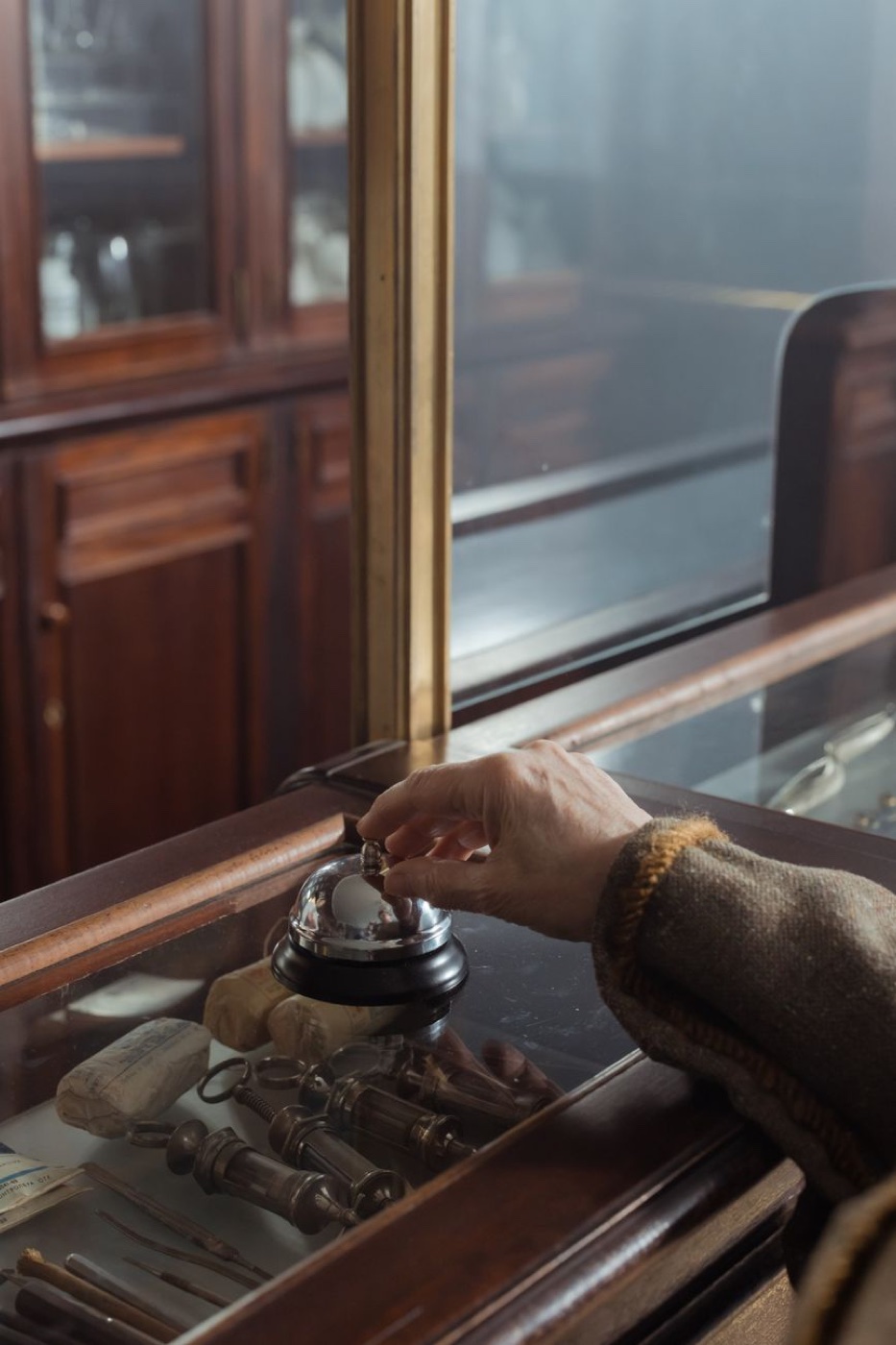 A hand pressing a chrome call bell on a wooden and glass shop counter in a dim vintage store