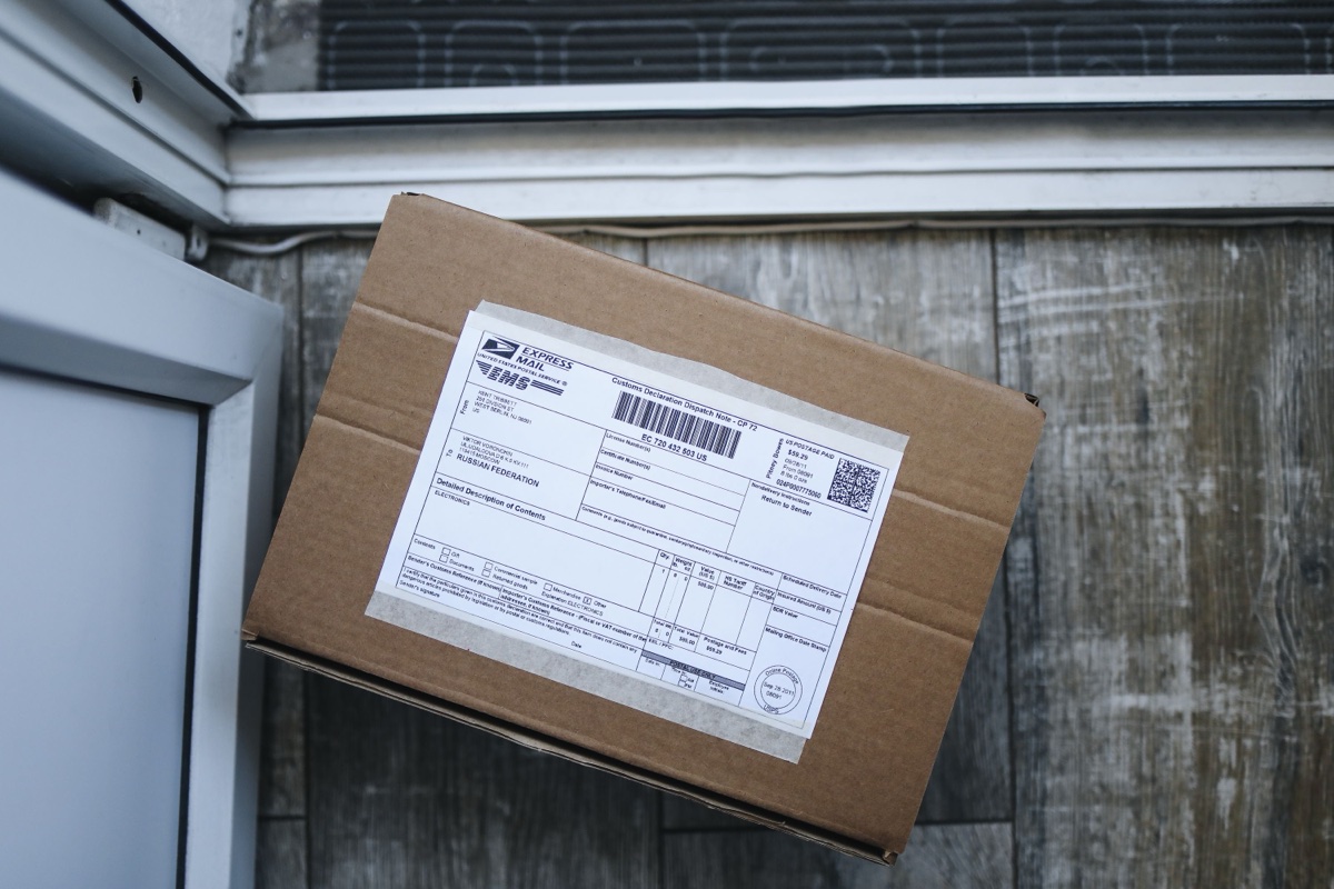 Cardboard parcel with an express mail label taped to it, sitting on a doorstep next to a screen door