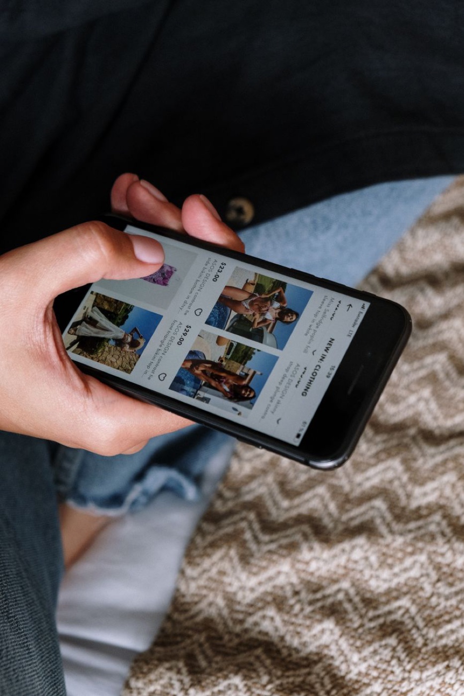 A hand holding a phone turned sideways, the screen filled with a grid of swimwear listings and prices