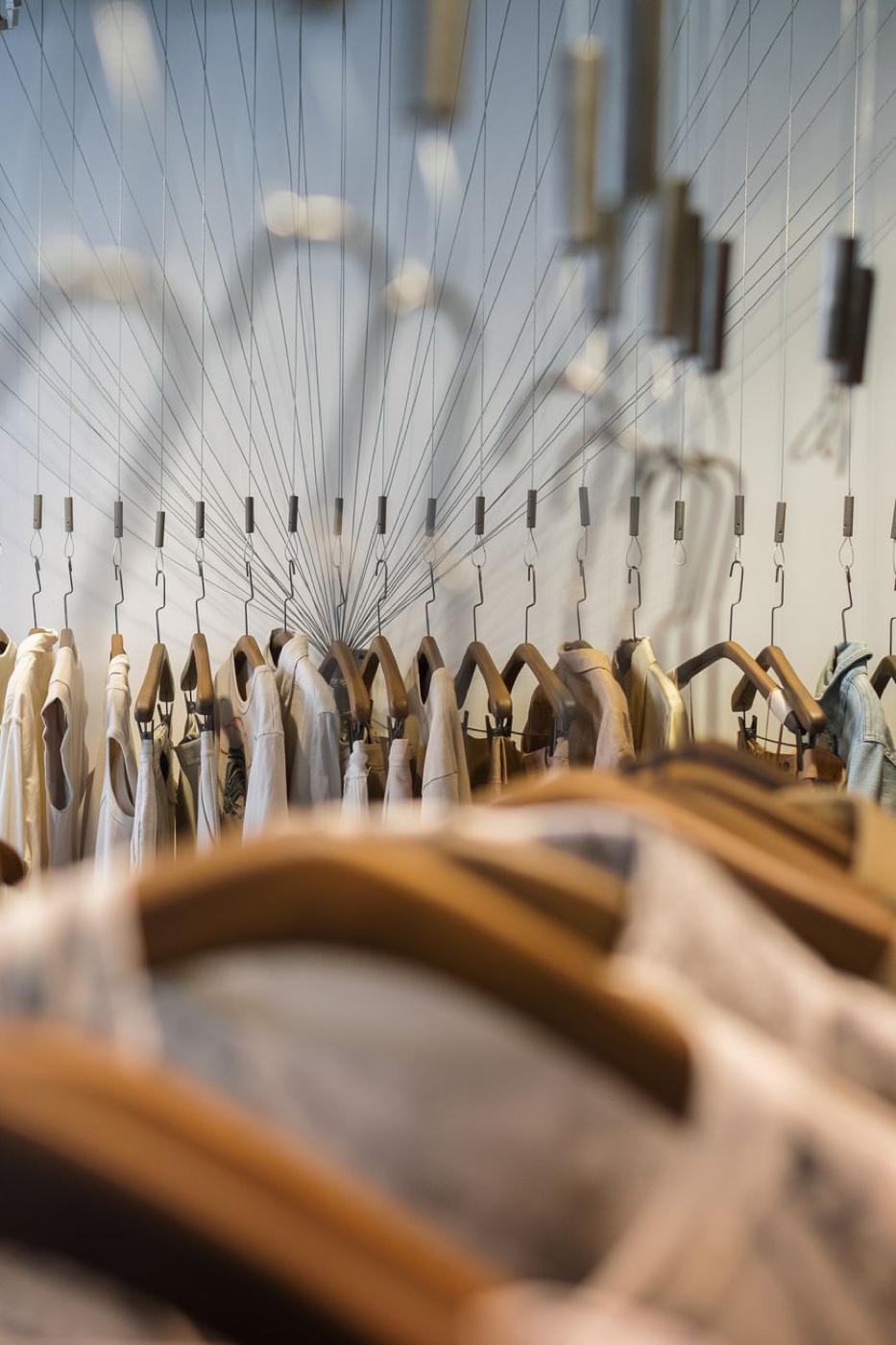 A long row of pale shirts and jackets on wooden hangers suspended from thin wires in a clothing shop