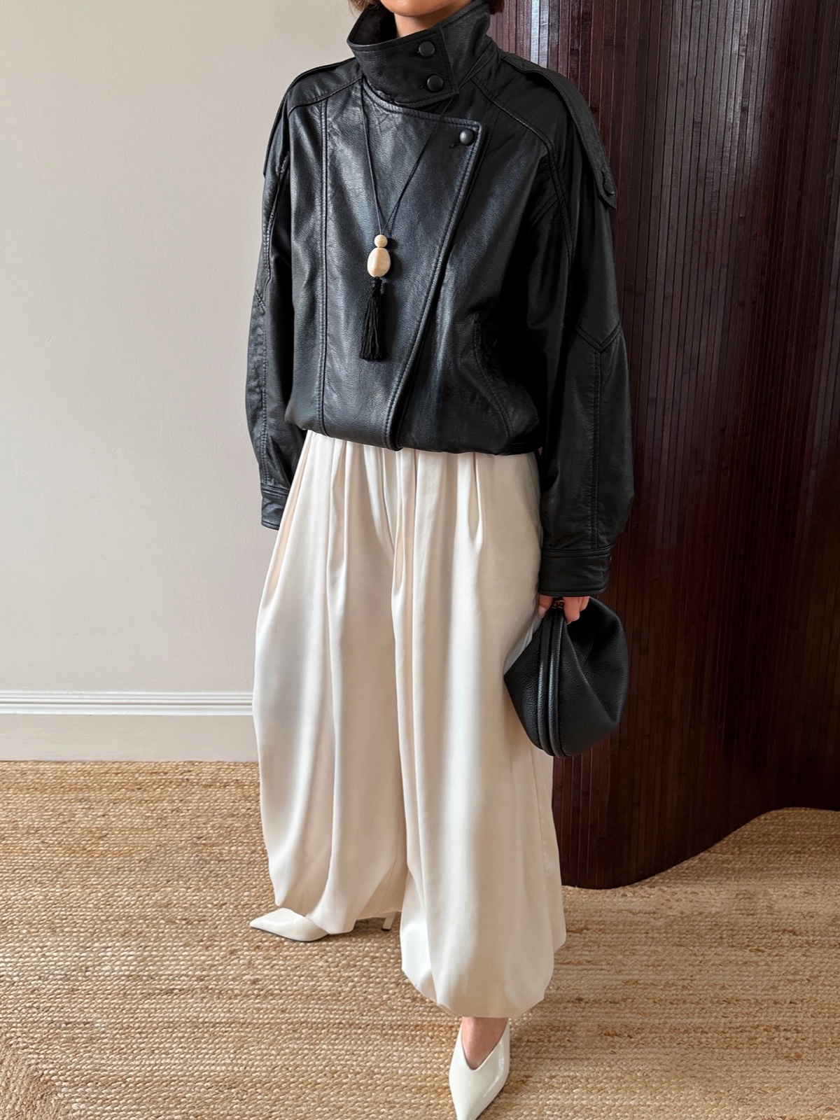 Cream satin balloon trousers styled with a black leather jacket and white heels, photographed indoors on a jute rug
