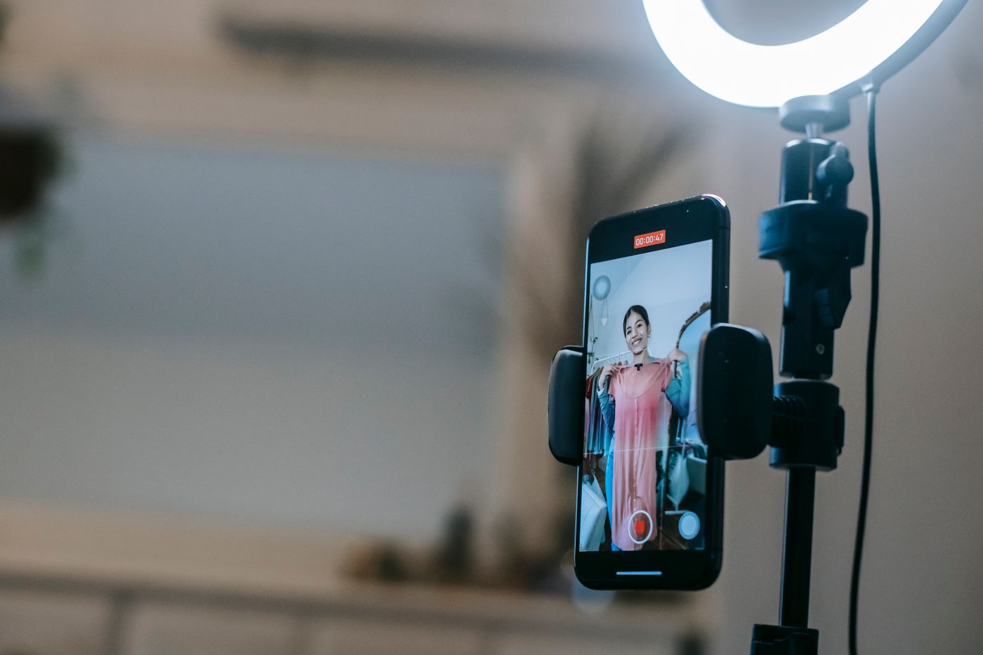 Smartphone mounted in a ring light rig recording a woman holding up a pink dress for a livestream