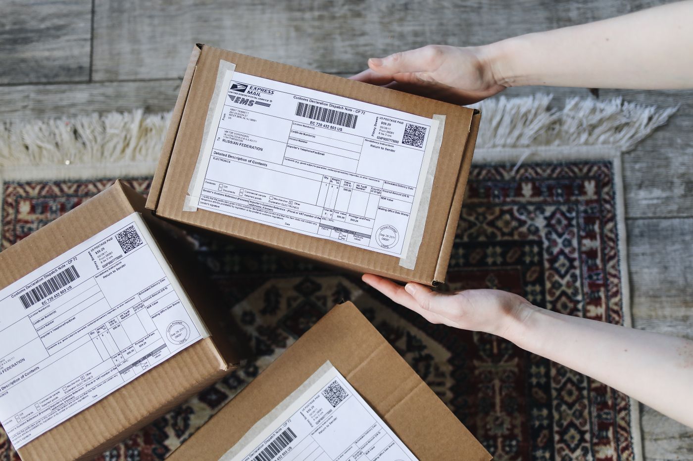 Hands holding a small cardboard box with an express mail label, two more labeled parcels below