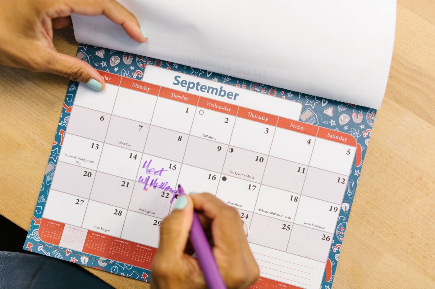 A hand writing on a September wall calendar with a purple pen, first week visible