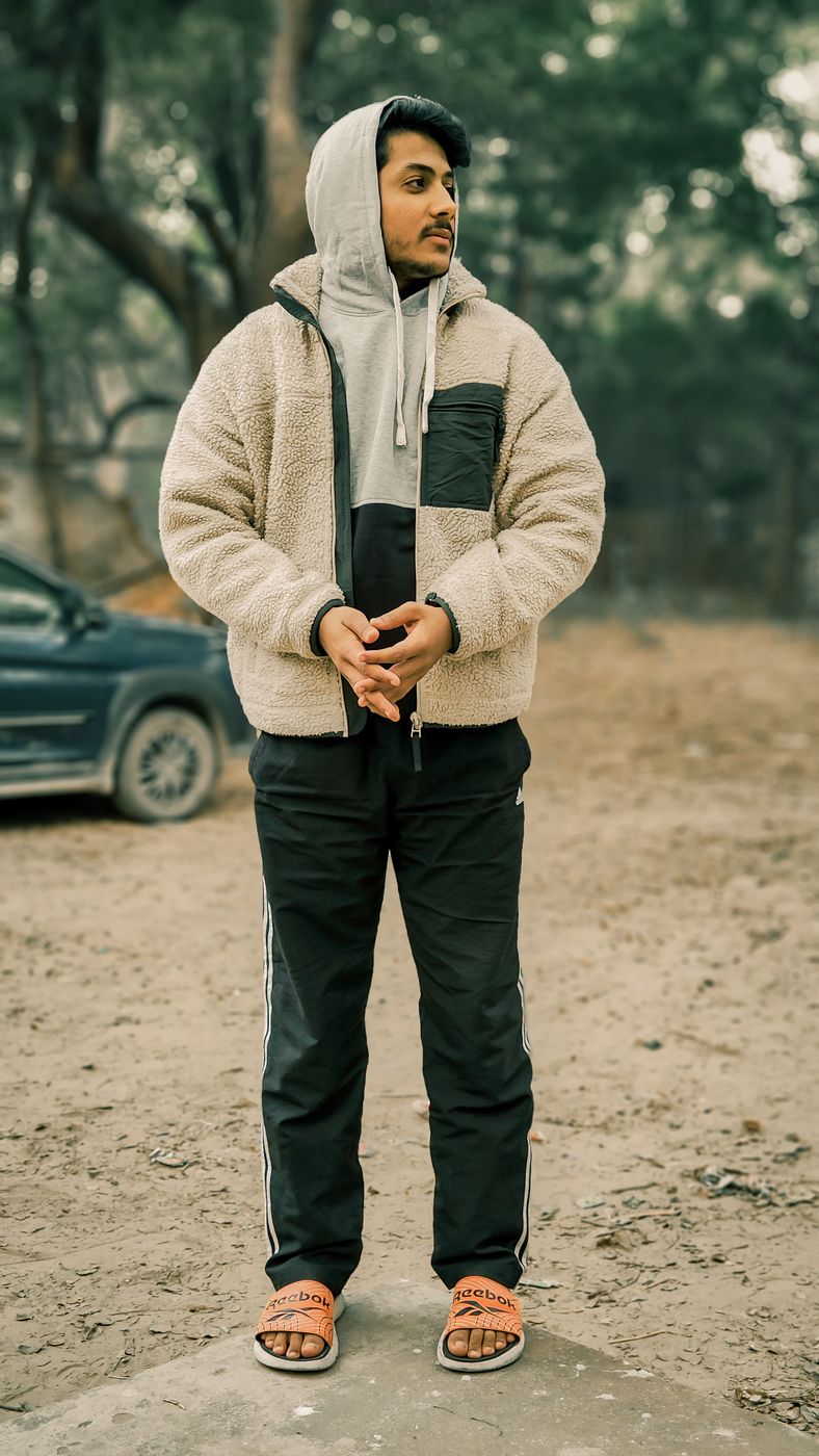 Man standing outdoors in a cream curly-pile zip jacket with a dark chest pocket, worn over a gray hoodie