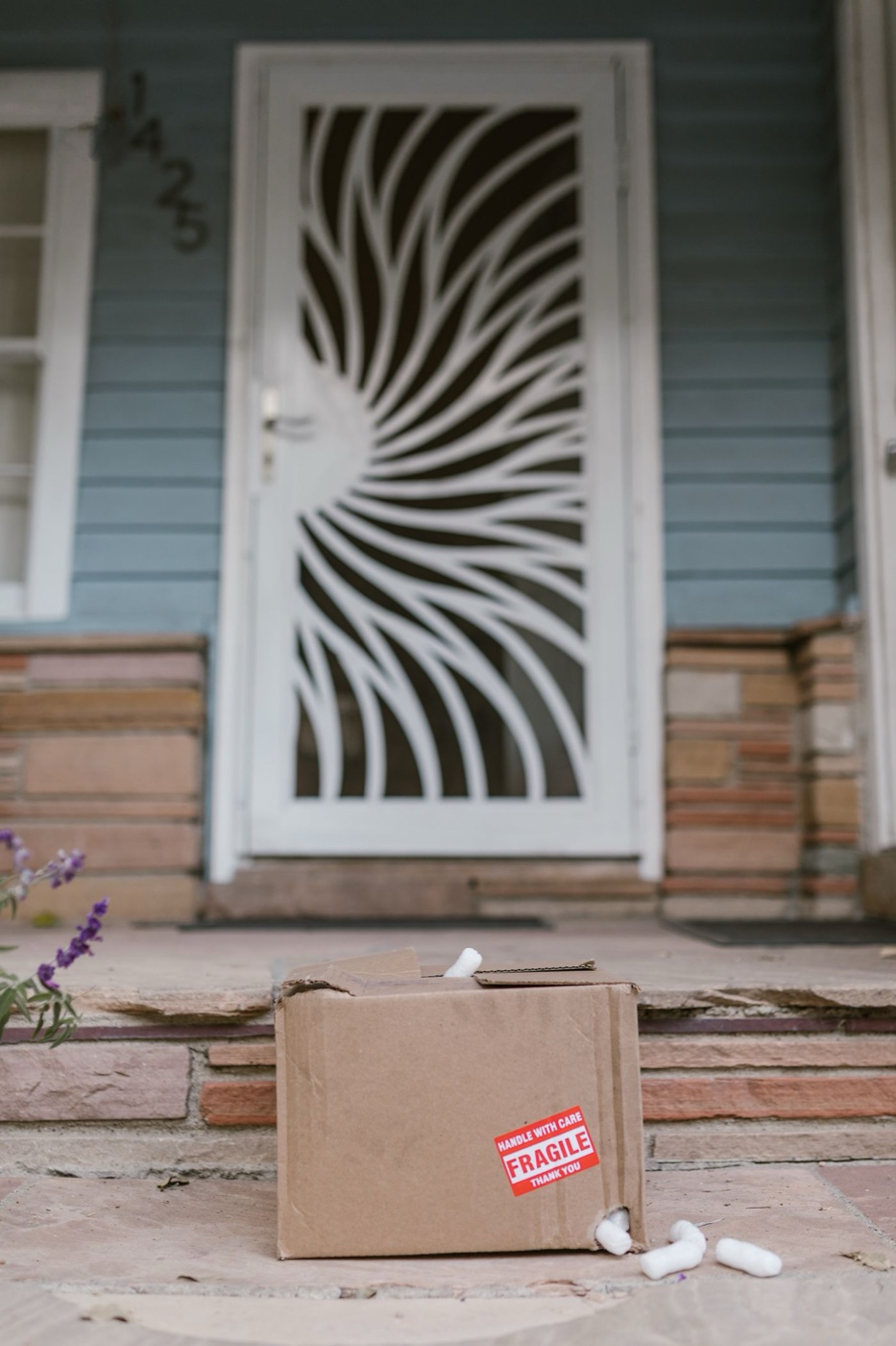 A crushed cardboard box with a red fragile sticker and spilled packing peanuts on porch steps