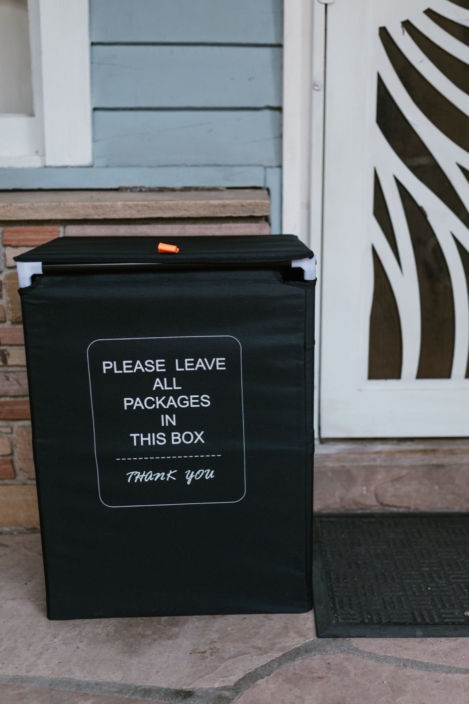 A black fabric parcel drop box labeled please leave all packages in this box beside a front door