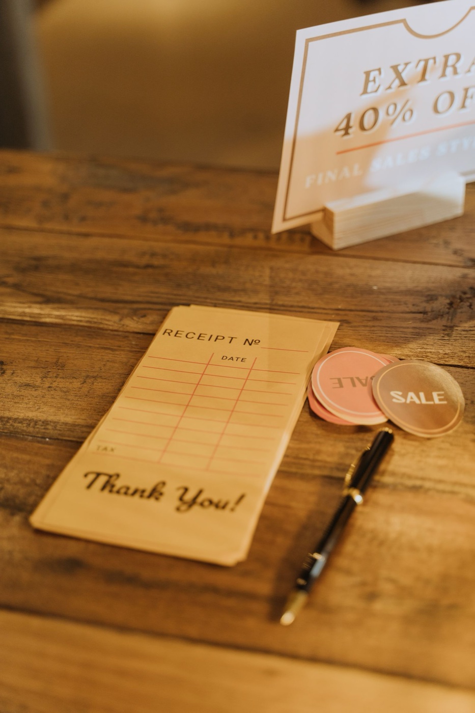 A carbon receipt pad, a stack of round SALE stickers and a printed card reading EXTRA 40 PERCENT OFF FINAL SALE STYLES on a wooden shop counter