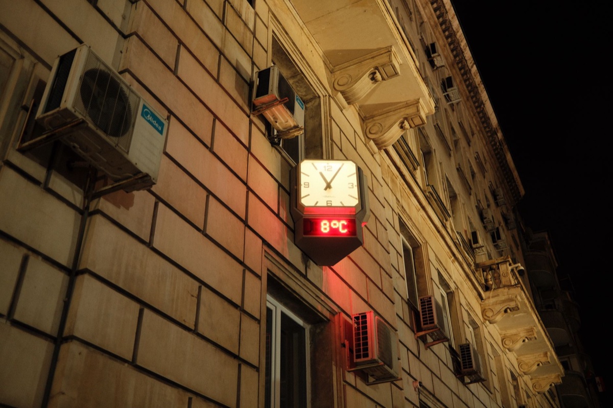 An illuminated street clock on a stone building facade showing 8 degrees Celsius in red digits at night