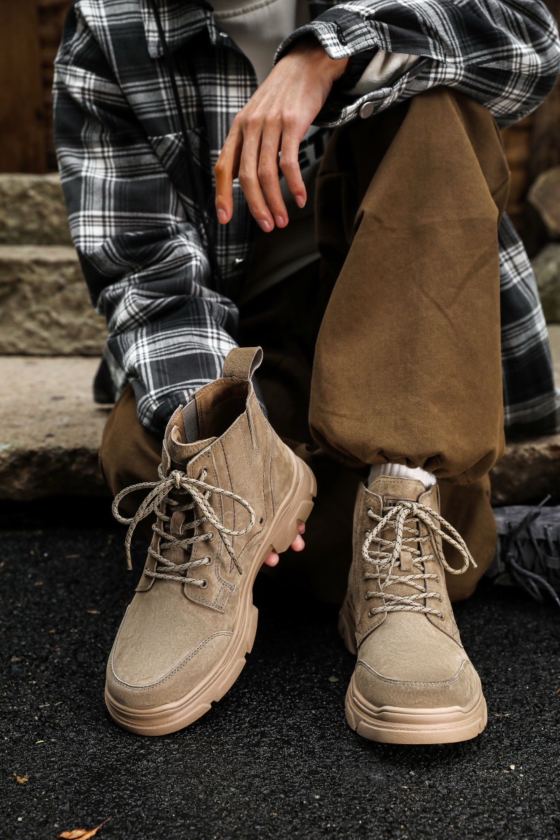 Person sitting on stone steps wearing beige suede lace-up boots with olive trousers and a plaid overshirt