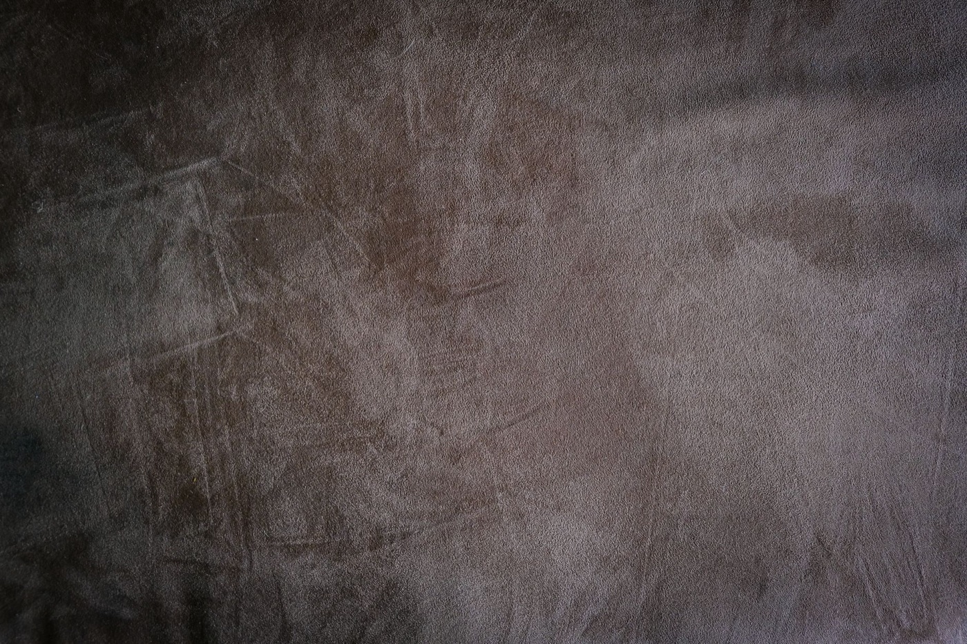 Extreme close-up of brown suede showing the raised nap, faint scratch marks and uneven shading across the surface