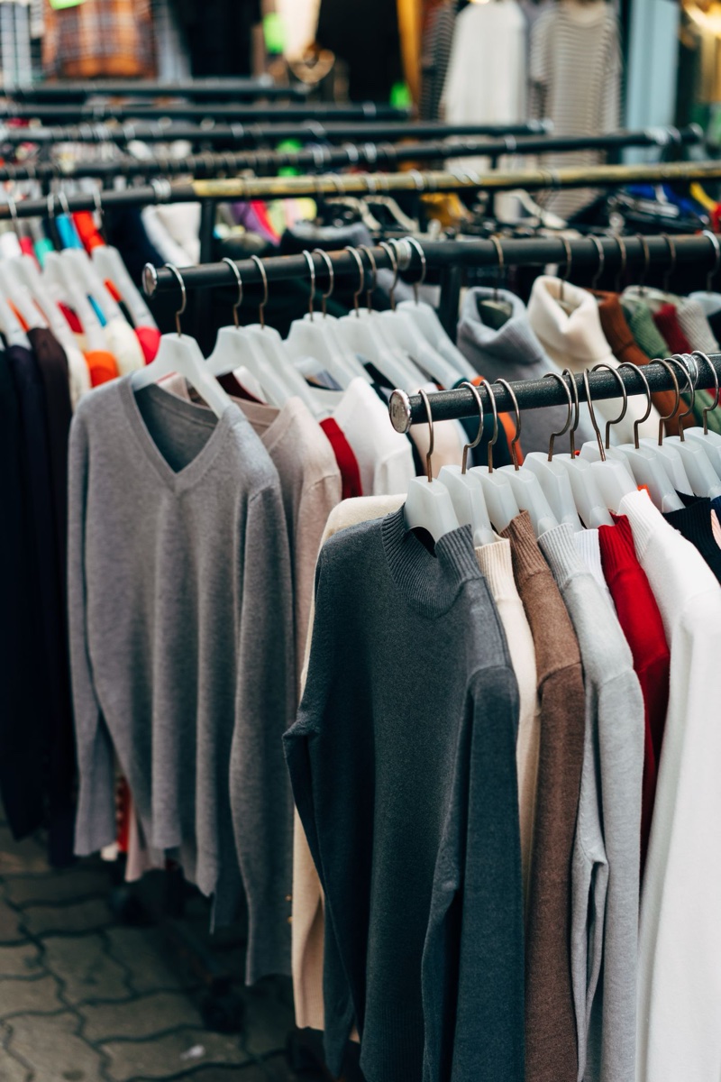 Rows of lightweight knit sweaters in grey, oatmeal, red and cream hanging on outdoor market racks under grey daylight