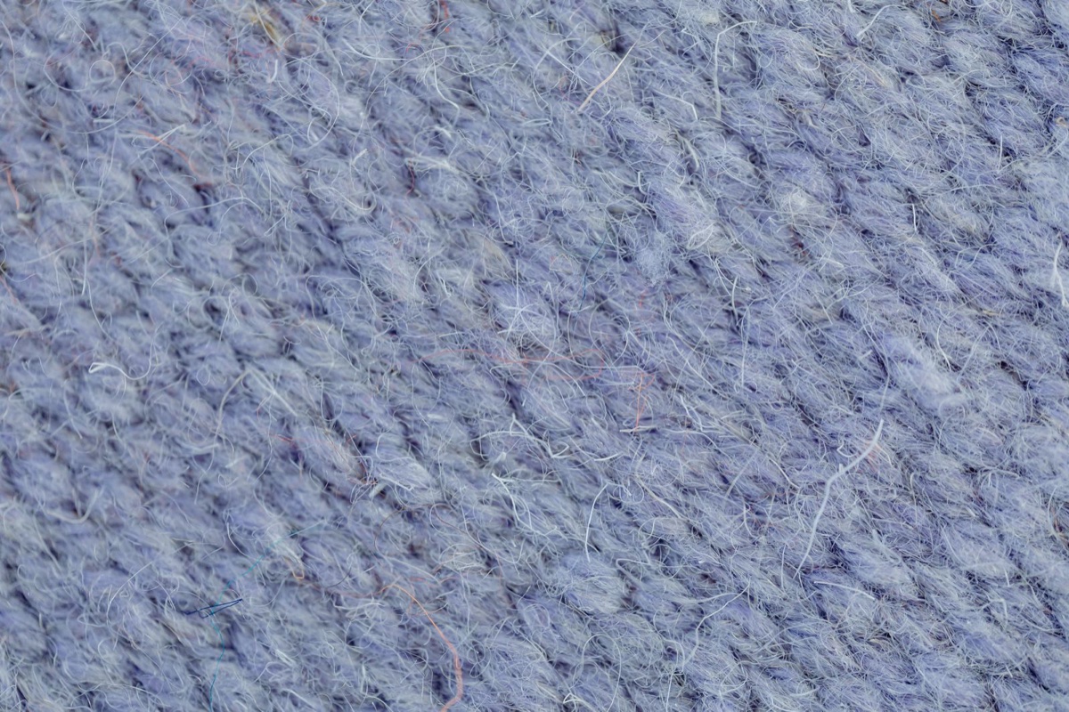 An extreme macro of pale blue wool fabric showing dozens of stray fiber ends rising off the surface of the weave