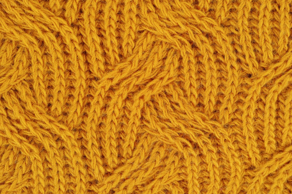 A macro of a mustard yellow cable knit sweater showing thick plied yarns twisted around each other
