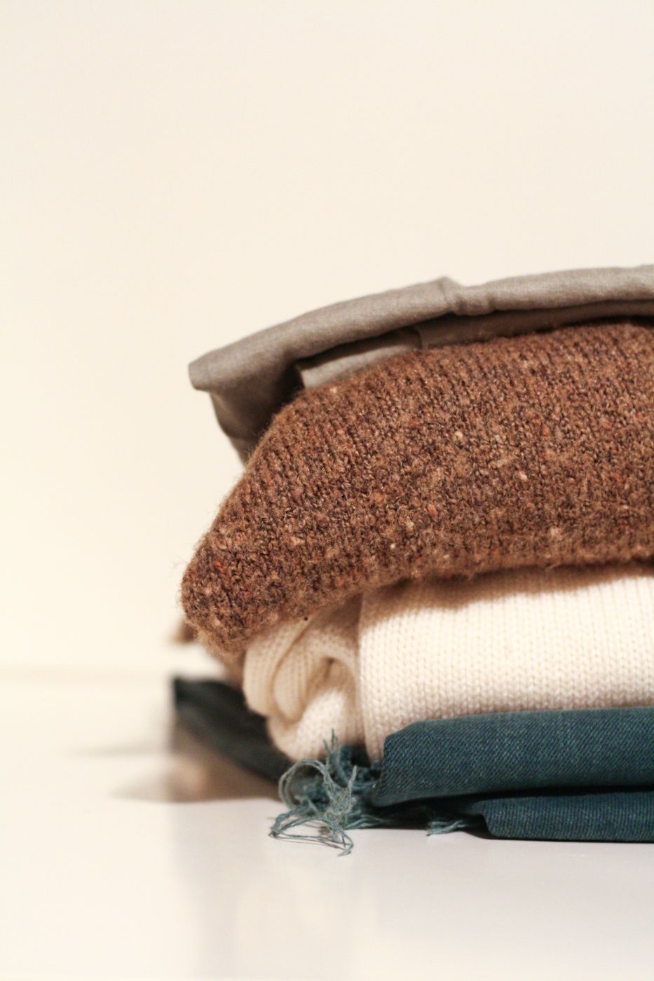 A small stack of folded knits, a flecked brown sweater on top of a cream one, sitting on folded teal denim