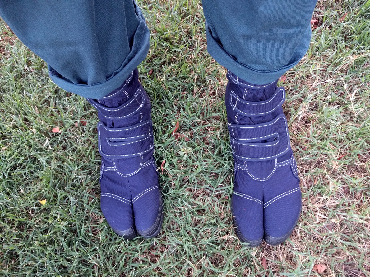 Two feet in new navy steel-toed tabi work boots with hook closures, standing on a lawn