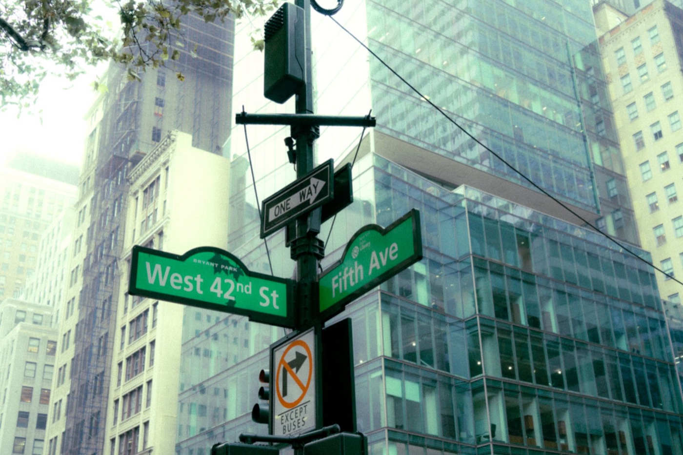 Green street signs for West 42nd Street and Fifth Avenue on a signal pole, glass towers behind