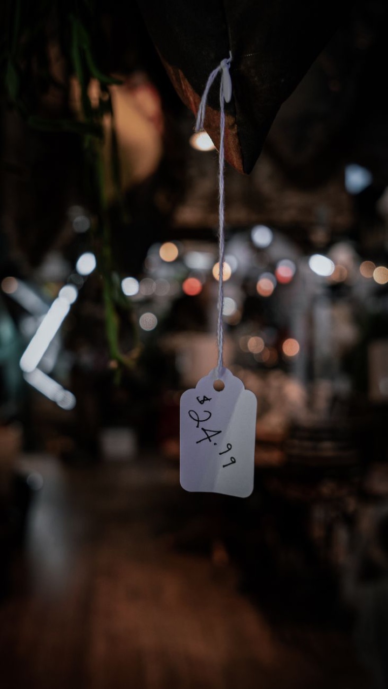 Handwritten $24.99 paper price tag hanging from string in a dim shop interior