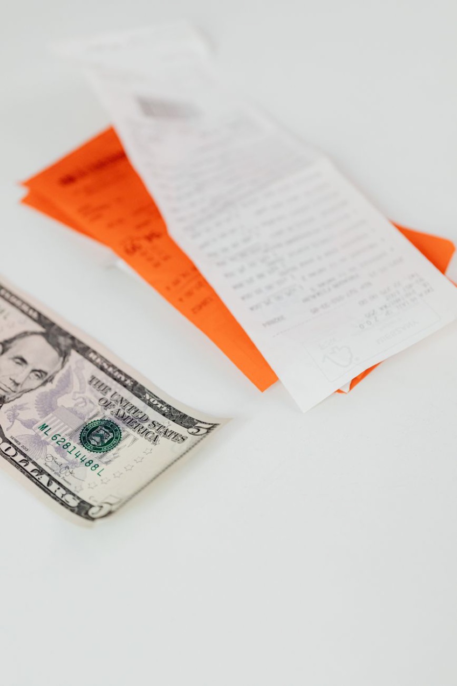 Store receipts and an orange return slip next to a five dollar bill on a white surface