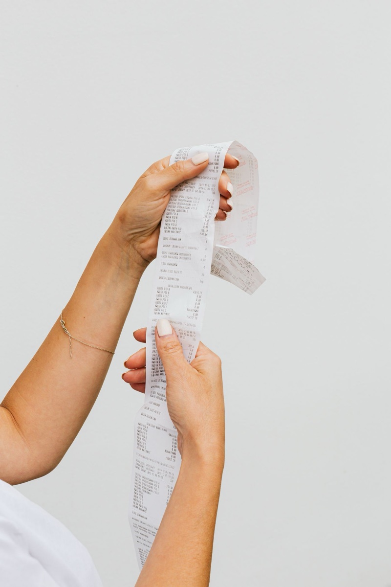 Two hands holding up a long paper register receipt against a plain white background