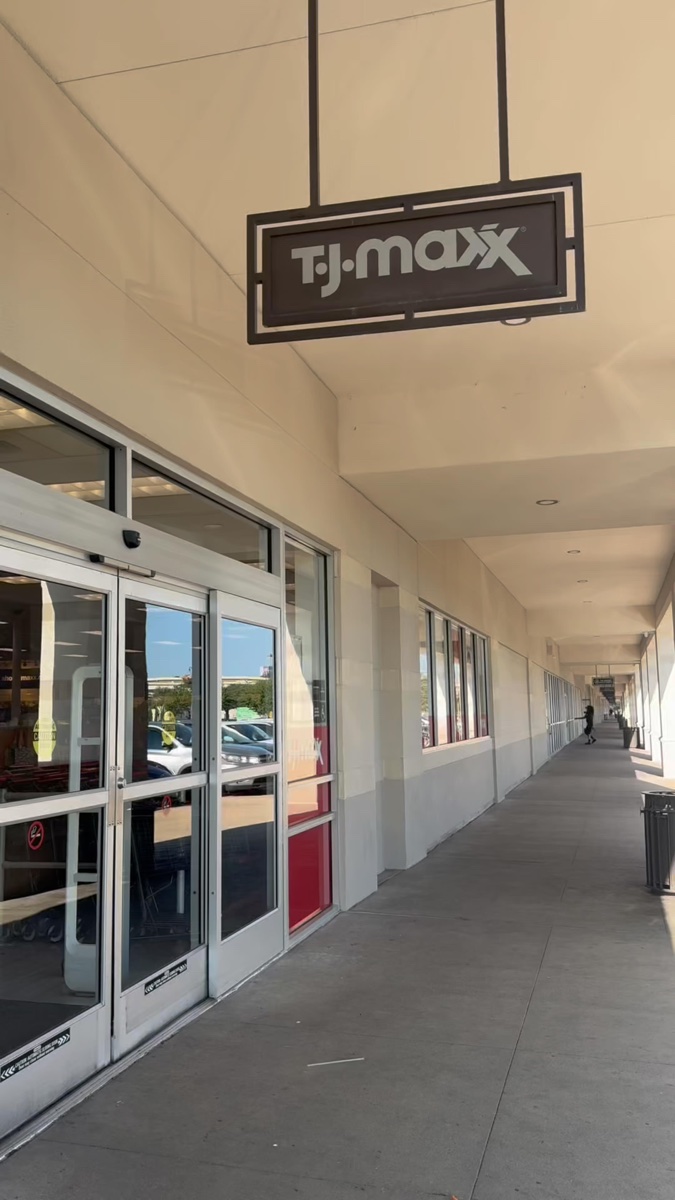 Sliding glass doors of a strip-mall T.J. Maxx under a covered walkway, the sign hanging overhead in afternoon sun