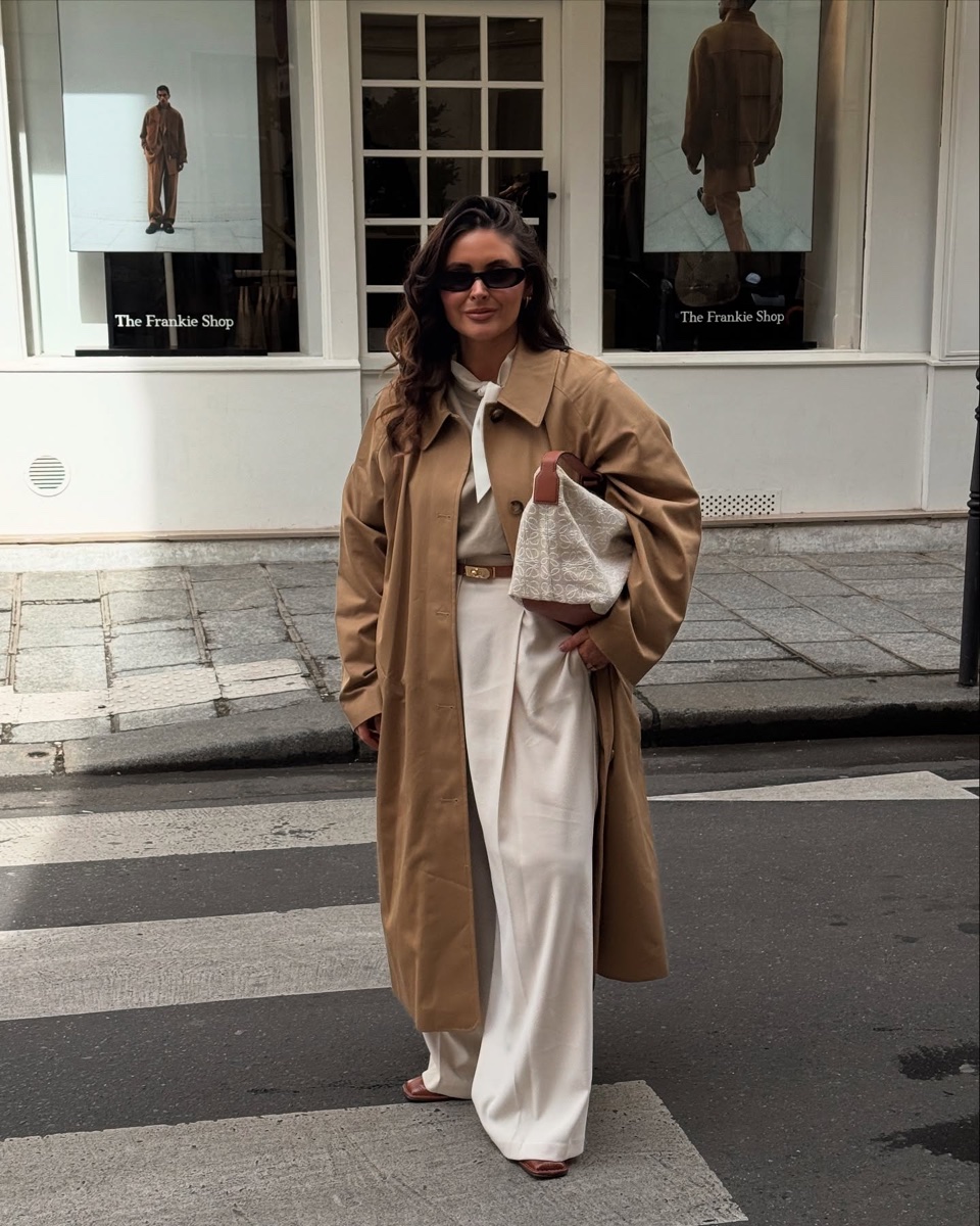 Woman in an oversized camel single-breasted trench and white trousers standing on a Paris crosswalk outside The Frankie Shop