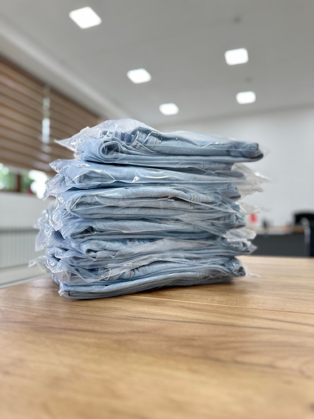 A stack of folded light wash jeans sealed in clear plastic polybags on a wooden table