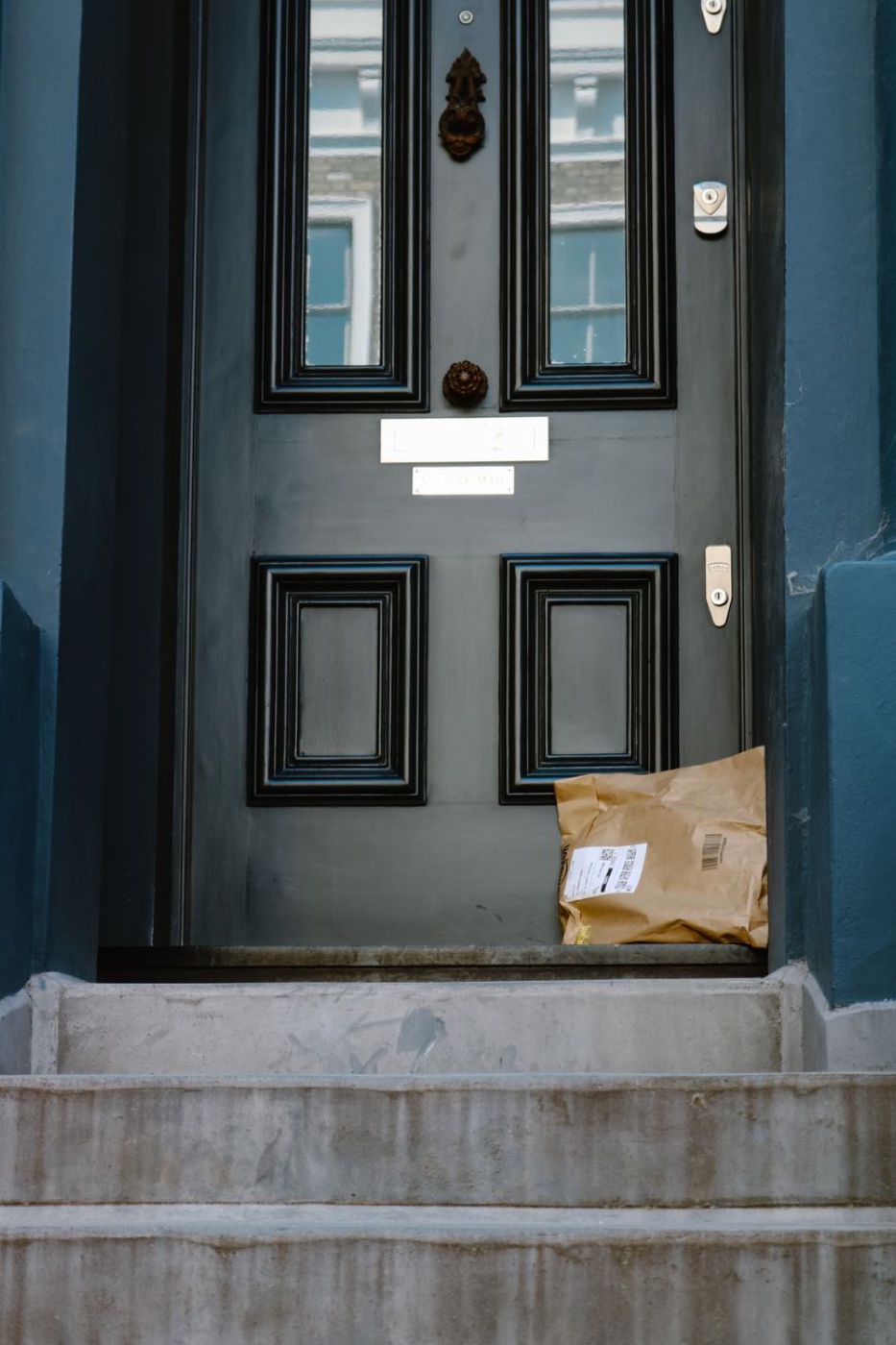 A paper delivery package leaning against a dark blue panelled front door at the top of stone steps