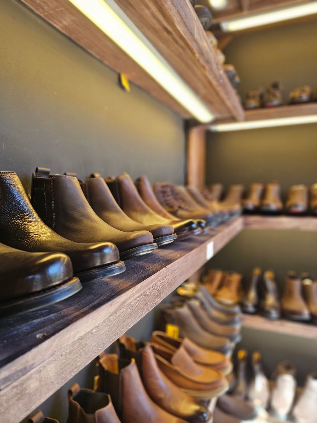 Rows of brown and black leather boots lined up on rustic wooden shelves under warm store lighting