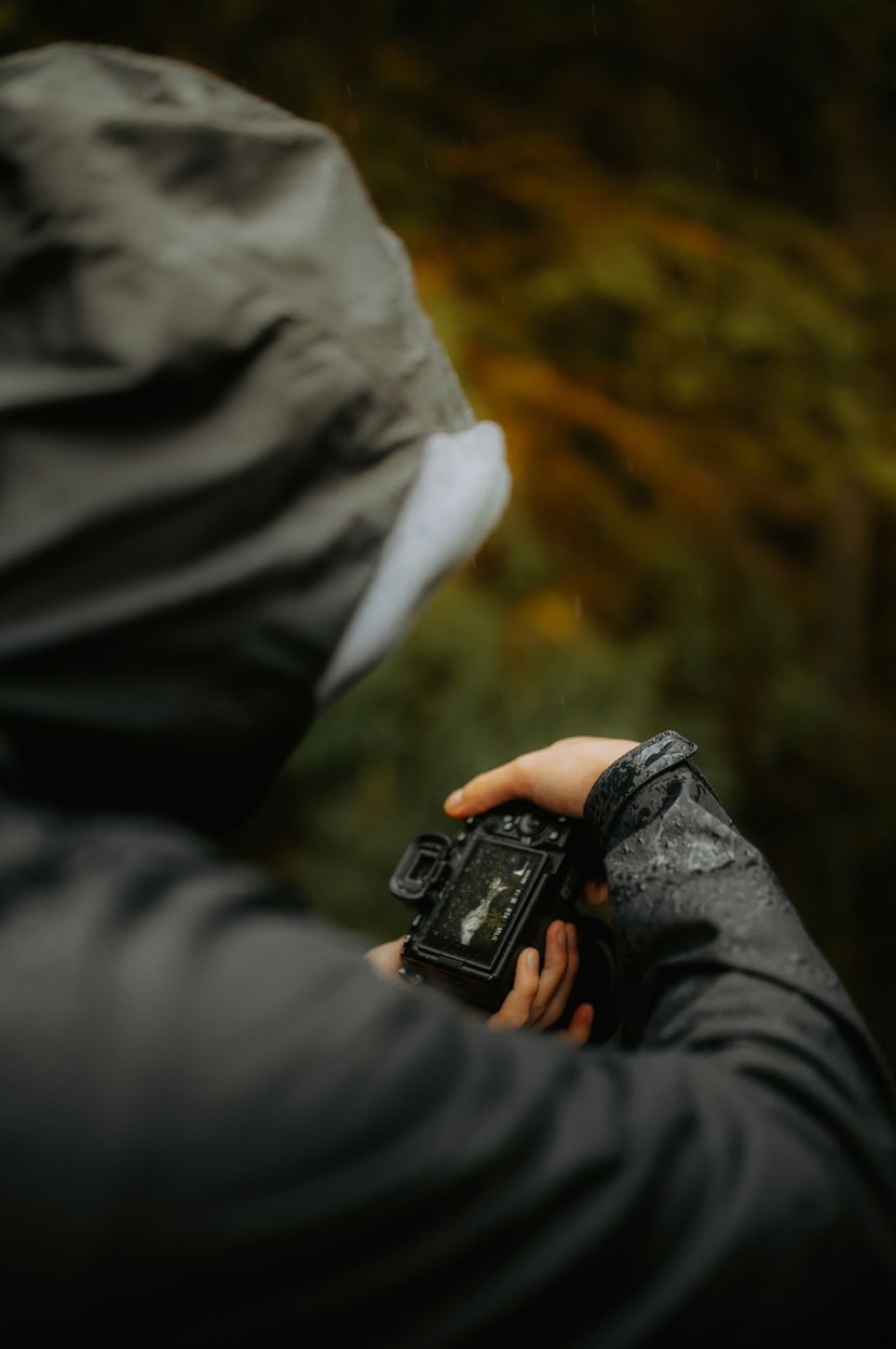 Close-up of water droplets beading on the wet grey sleeve of a hooded shell jacket held up to a camera