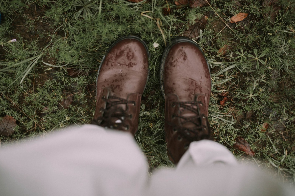 Rain-spattered brown smooth leather boots seen from above on wet grass and fallen leaves