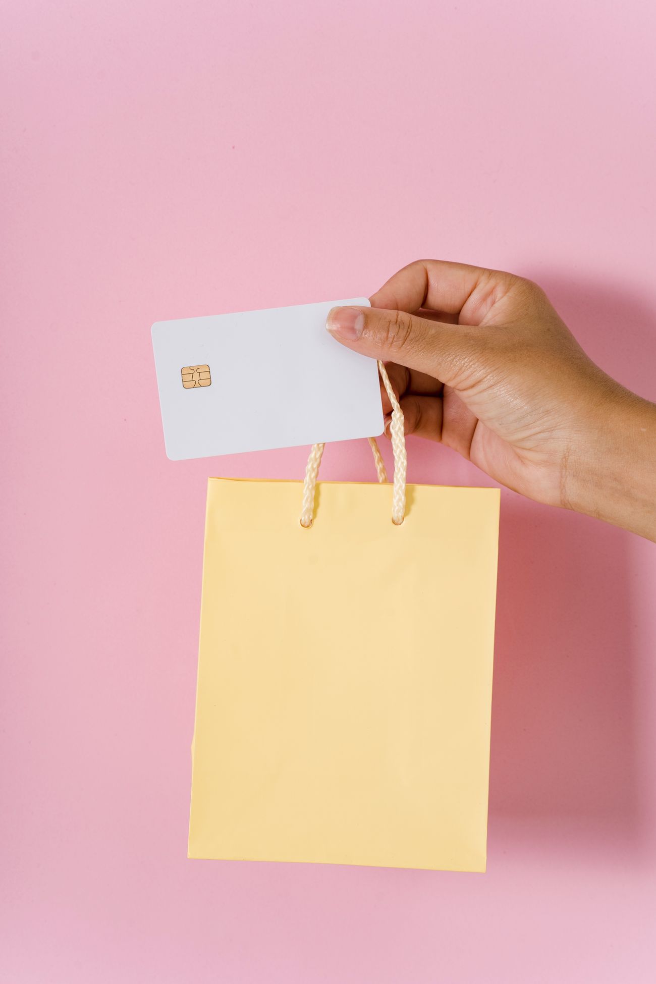 A hand holding a blank white chip card above a small yellow paper shopping bag