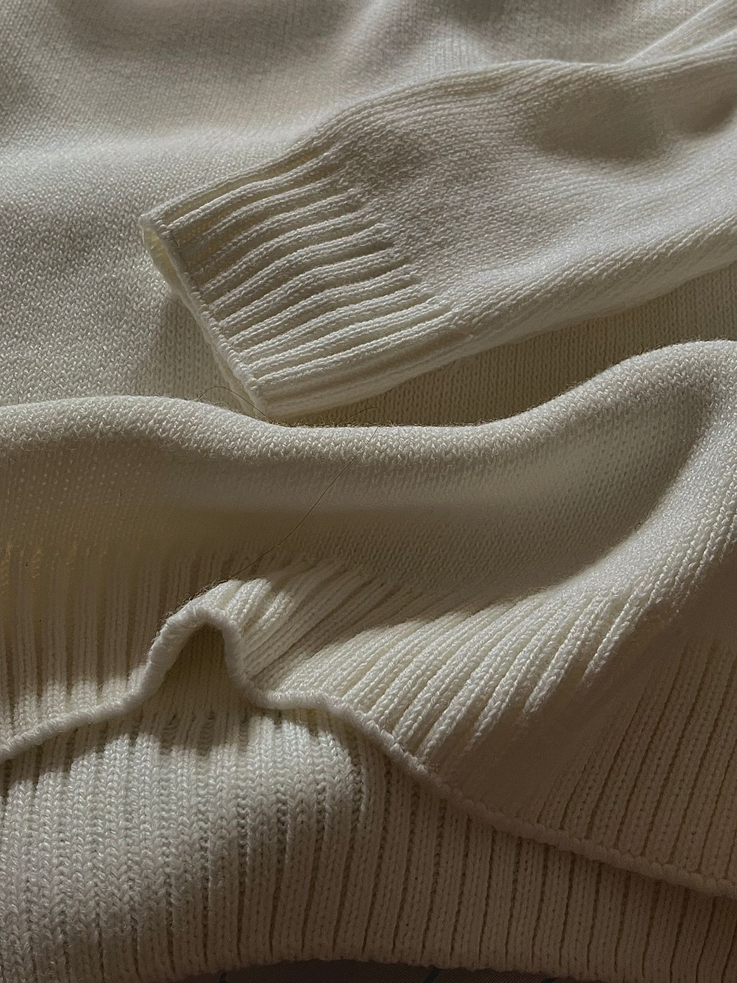 A close-up of a cream knit sweater with ribbed cuffs and hem folded in soft light