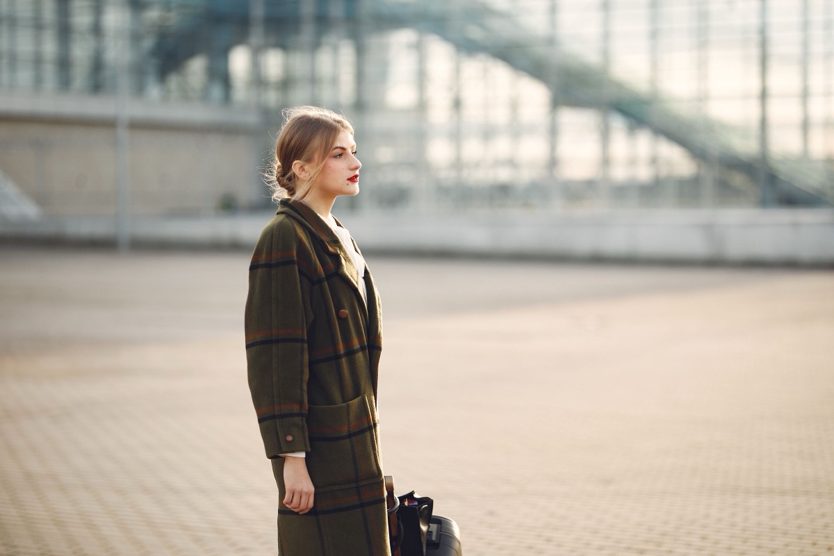 Woman in profile wearing an olive windowpane check coat outside a glass building