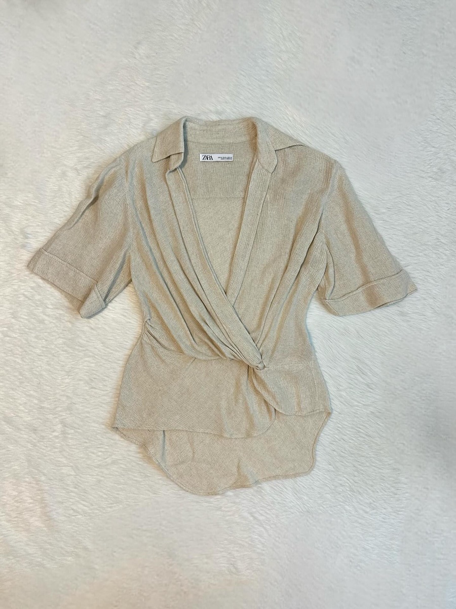A beige linen knit wrap blouse with its Zara tag laid flat on a white textured blanket