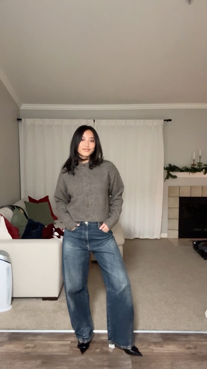 A woman in a taupe cropped cardigan and baggy jeans standing in a living room during a Zara haul